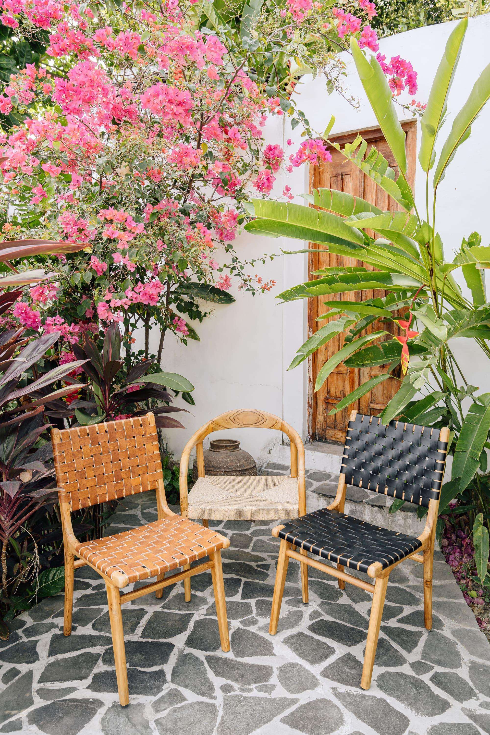 Handmade wooden chairs and natural woven bench in a tropical garden with pink flowers, Kayu Living
