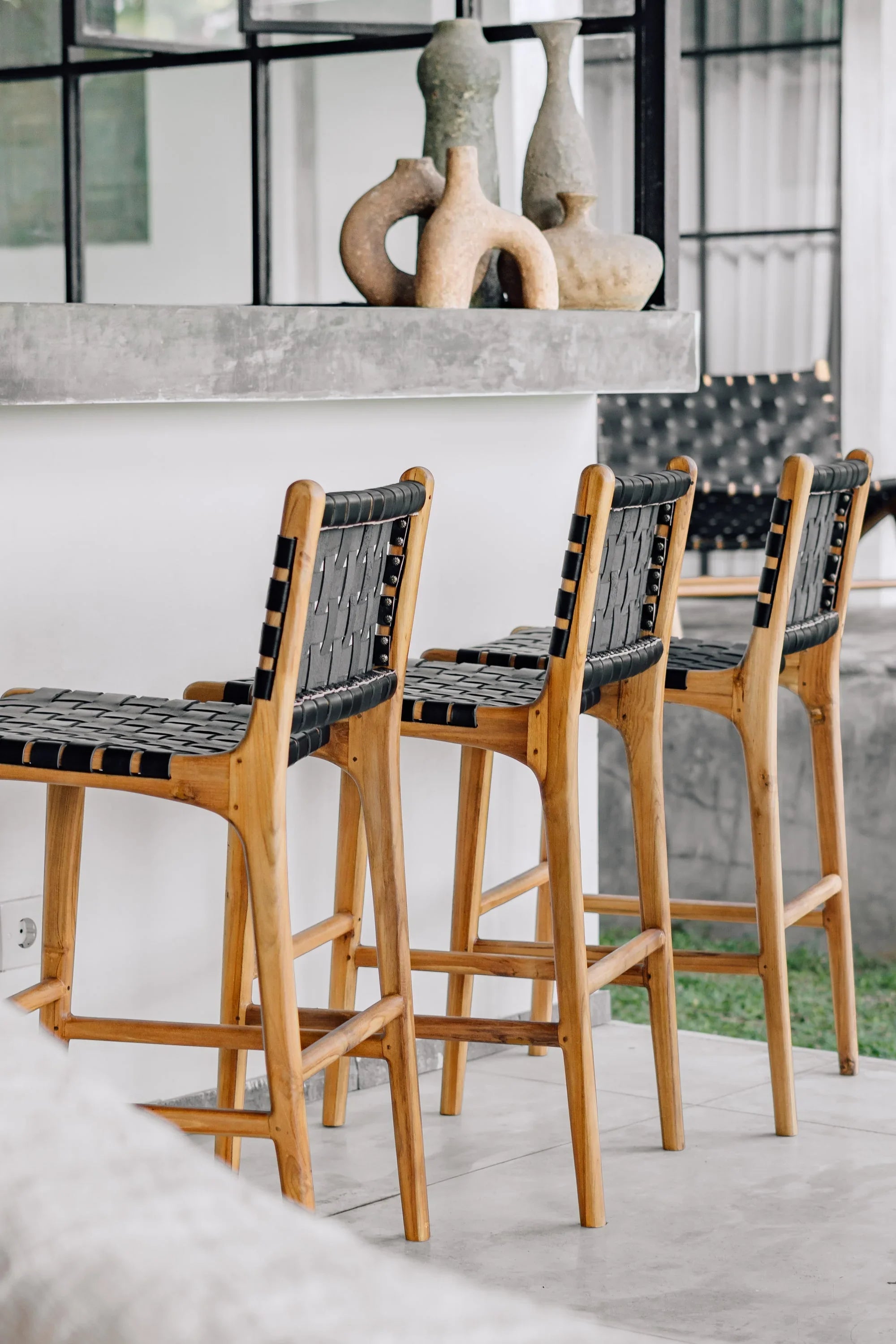 Handcrafted wooden bar stools with black woven seats by a modern concrete counter, Kayu Living