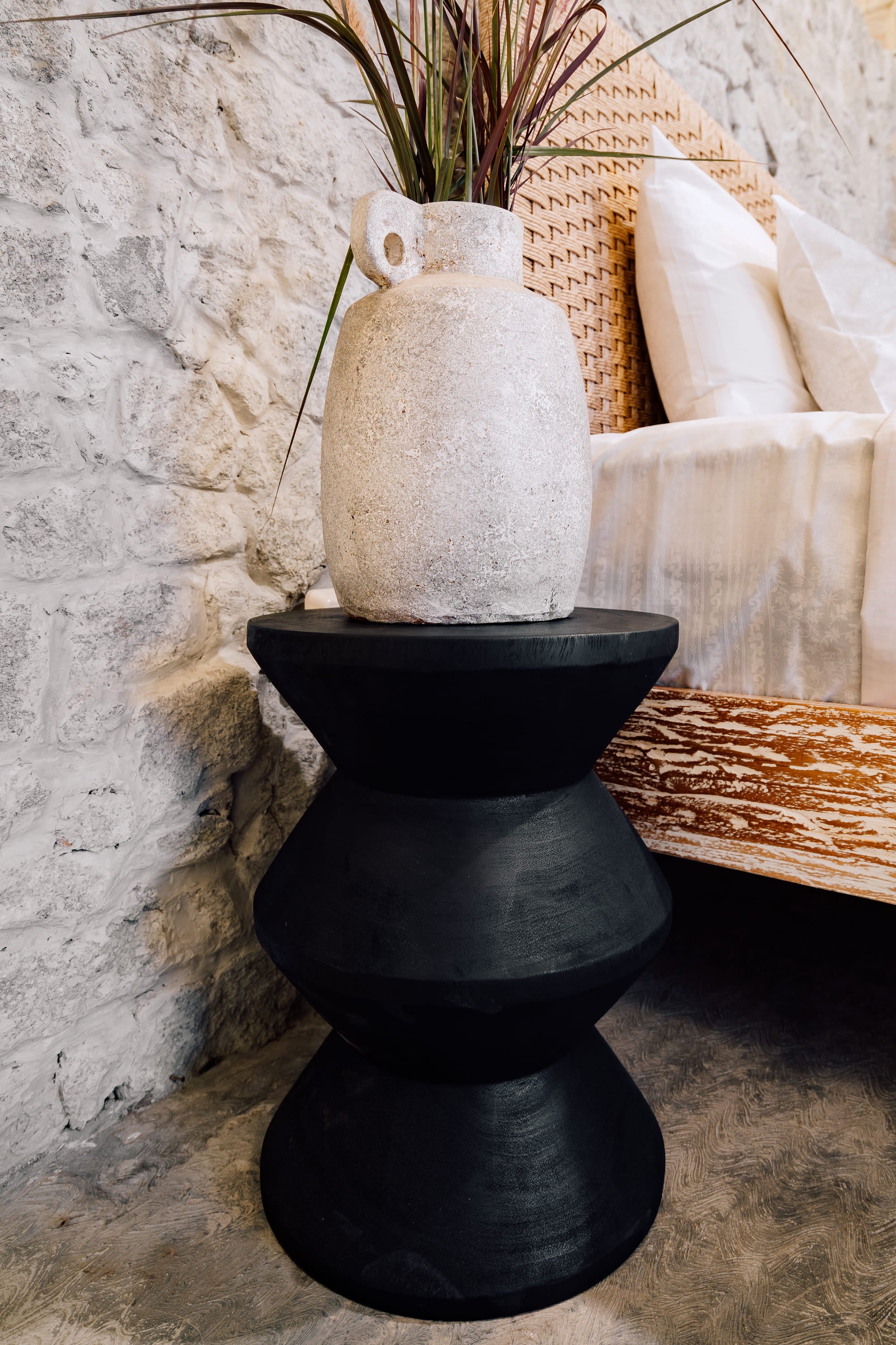 Black pedestal table with a textured white vase on a stone surface