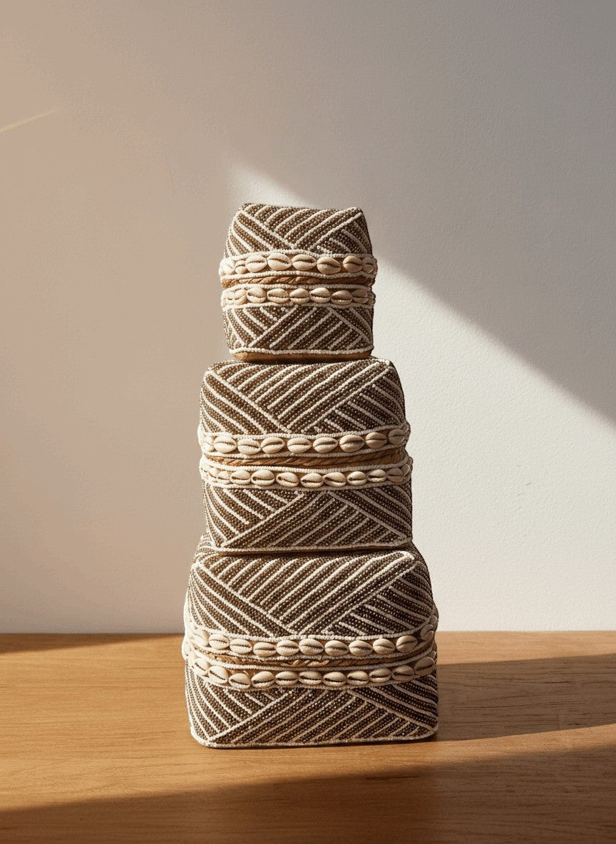 Kayu Living handmade beaded boxes in gold and white with shell accents, stacked for display.