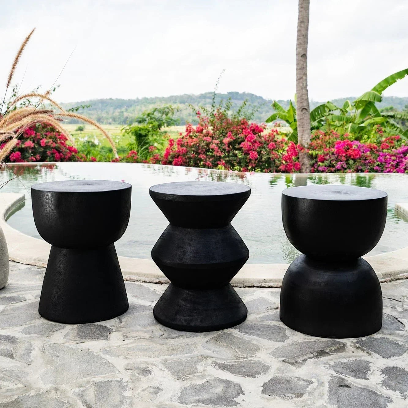Kayu Living black solid suar wood stool with cupped top and hourglass shape, unique handcrafted design.