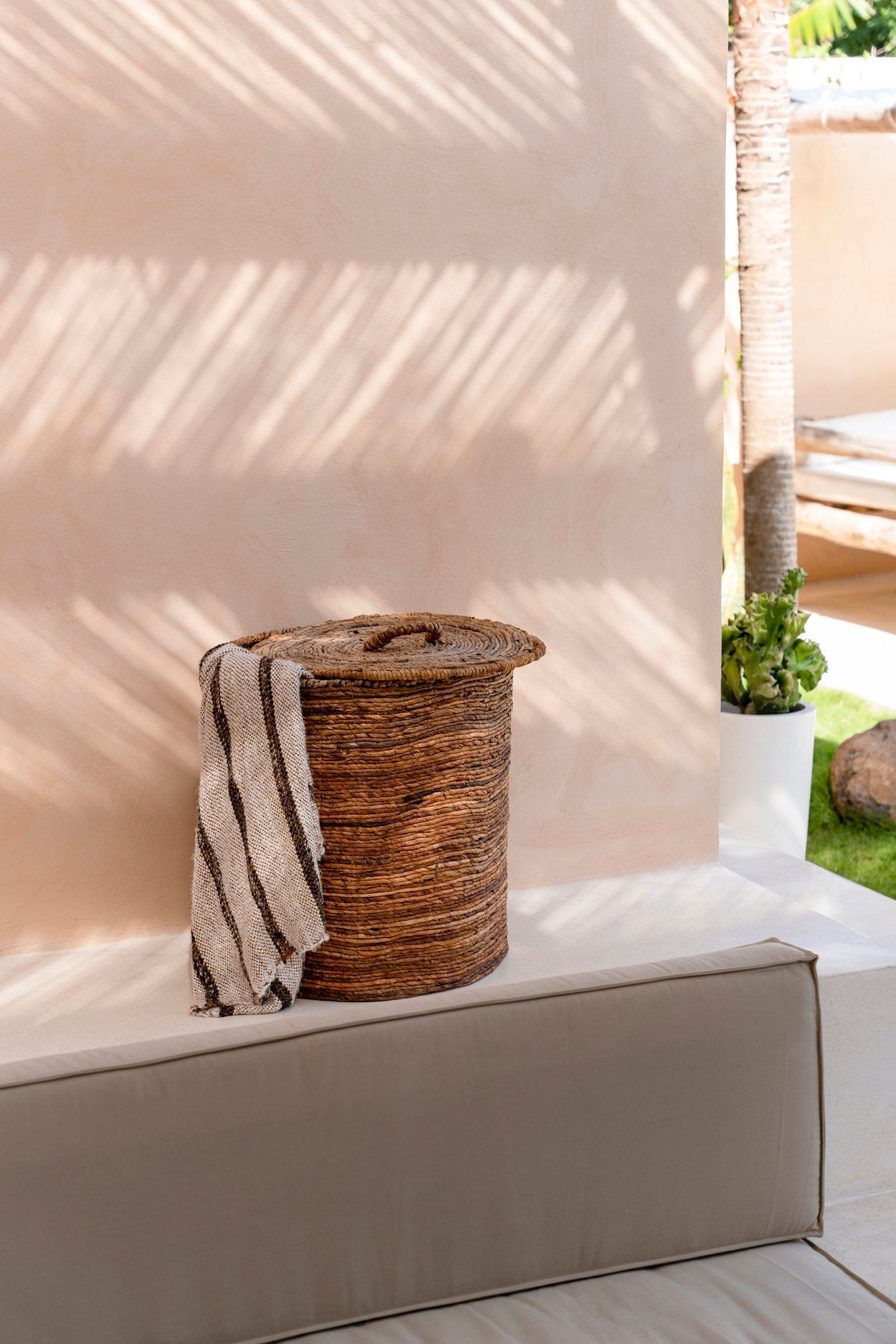Kayu Living hand-woven cotton plaid in Bohemian White with brown stripes draped over a rustic woven storage basket.