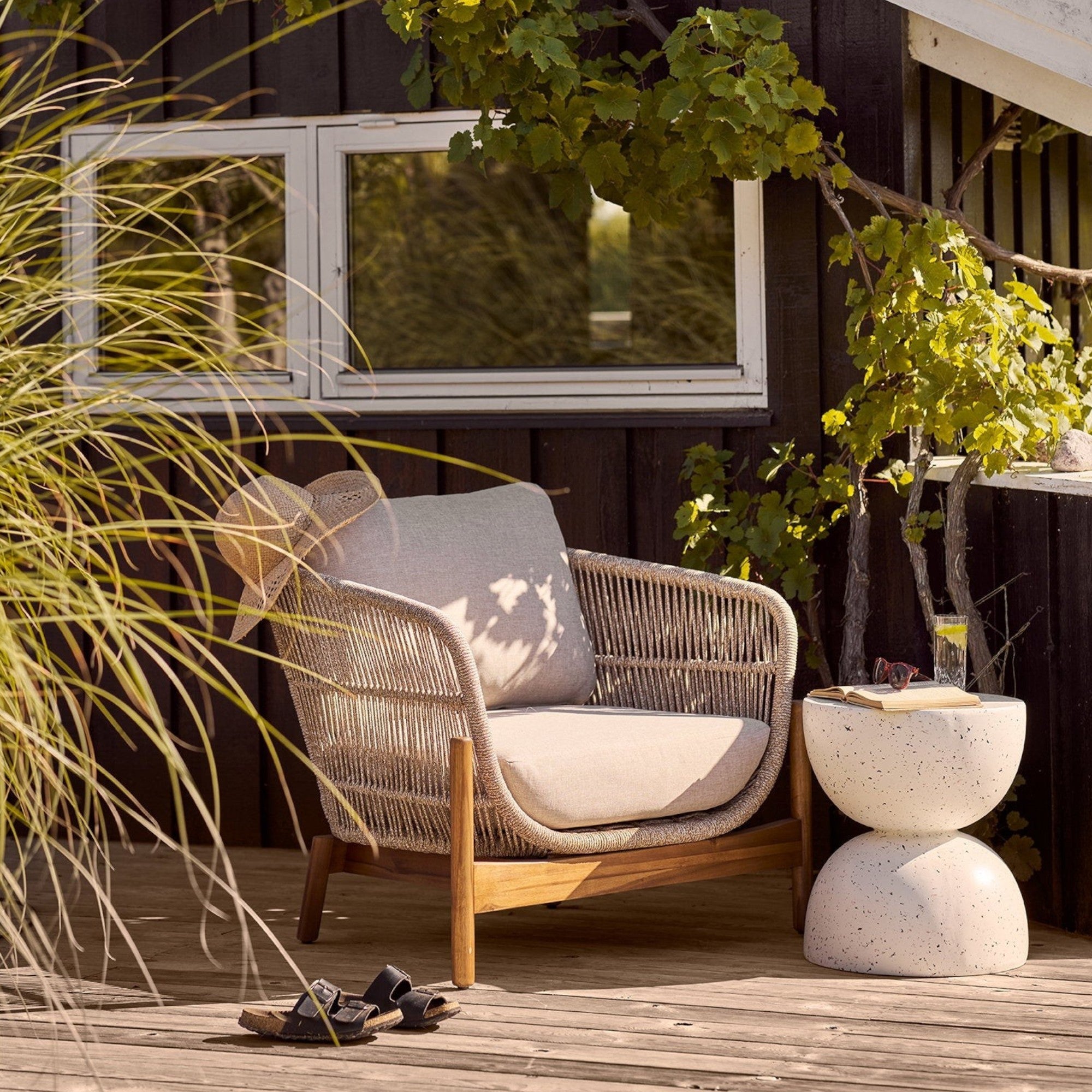 Kayu Living Bonita off-white fiberclay side table with a terrazzo finish on a wooden deck next to a lounge chair.