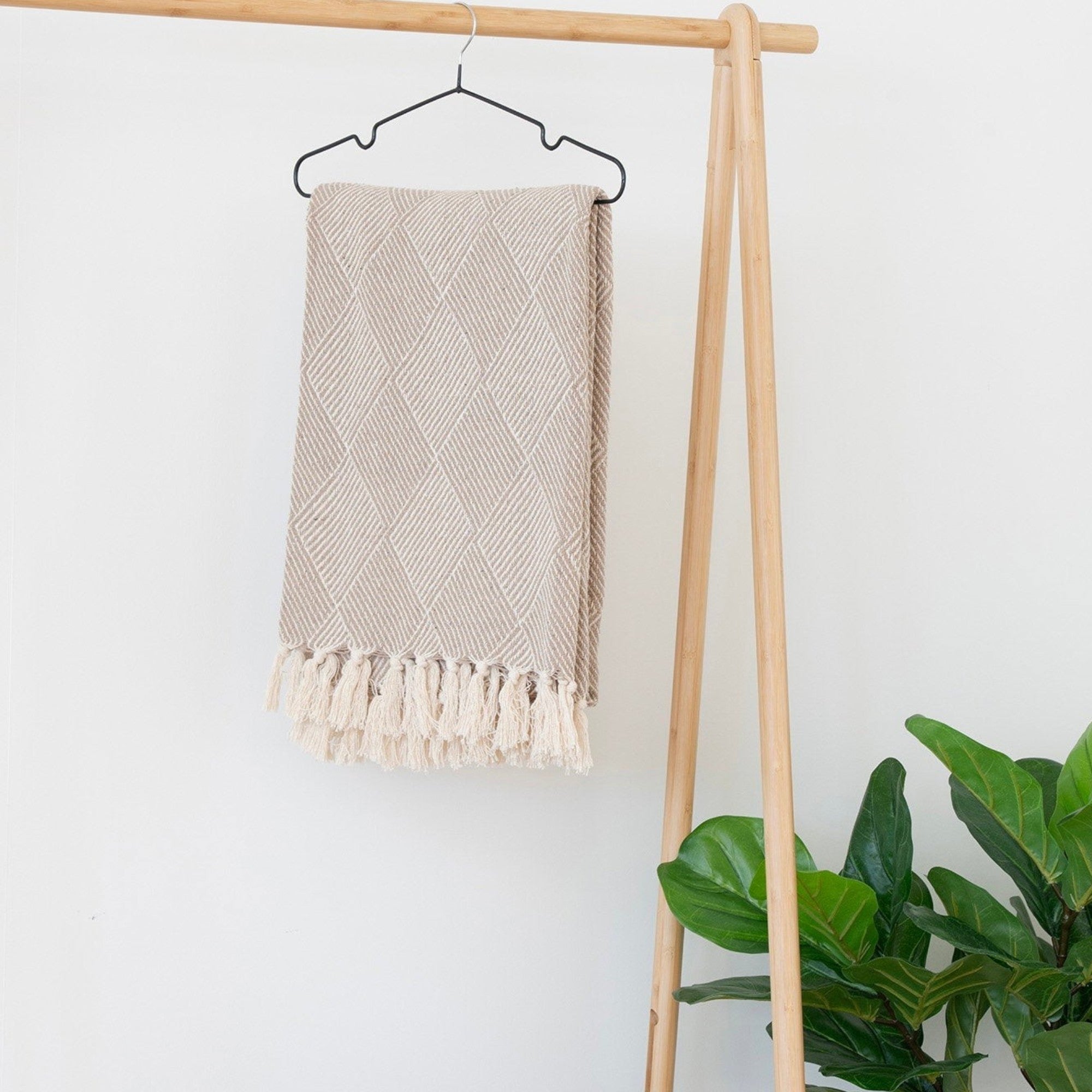 Kayu Living Bursa Plaid taupe throw blanket with diamond pattern and fringe, hanging on a wooden rack.