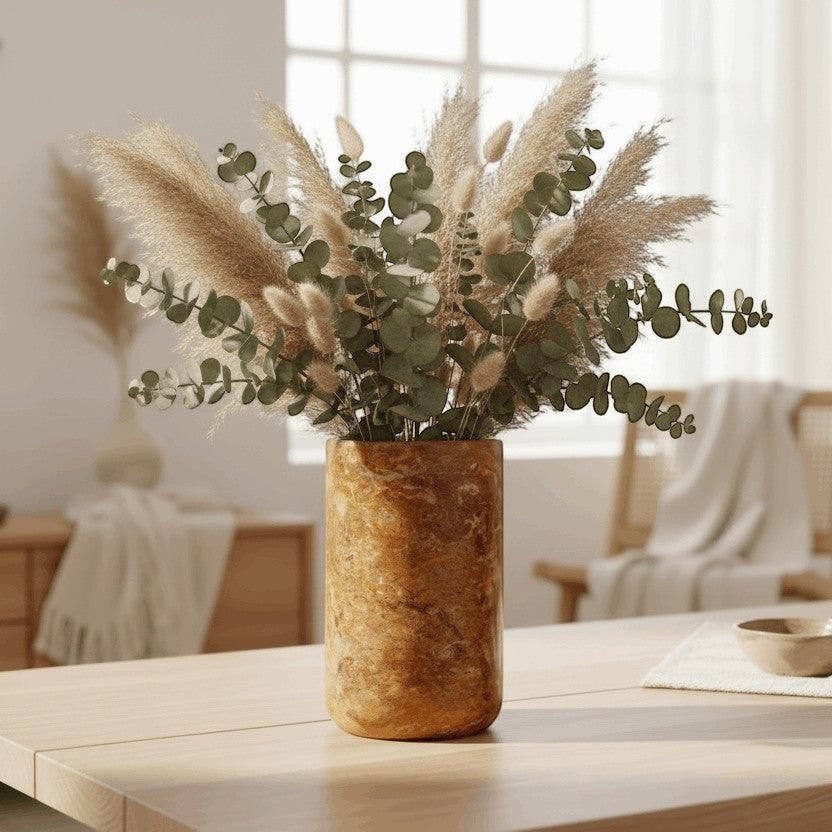 Kayu Living caramel onyx stone wine cooler and vase with unique veining, holding dried pampas grass and eucalyptus.