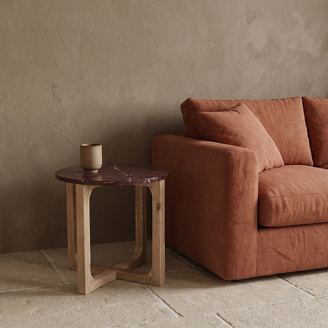 Kayu Living burgundy marble side table with white veins and mango wood cross-leg base next to a rust-colored sofa.