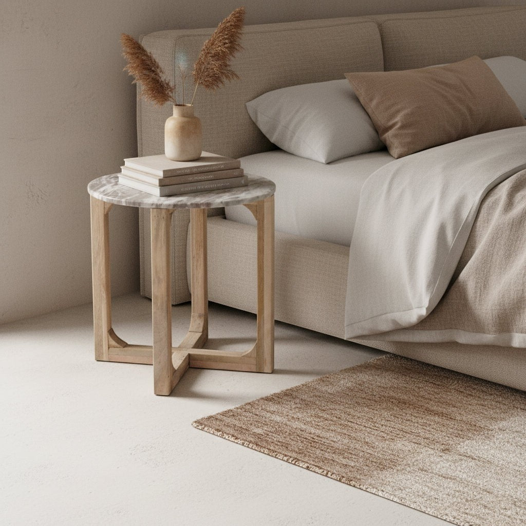 Kayu Living round Fantasy Brown marble side table with natural mango wood base next to a beige upholstered bed.