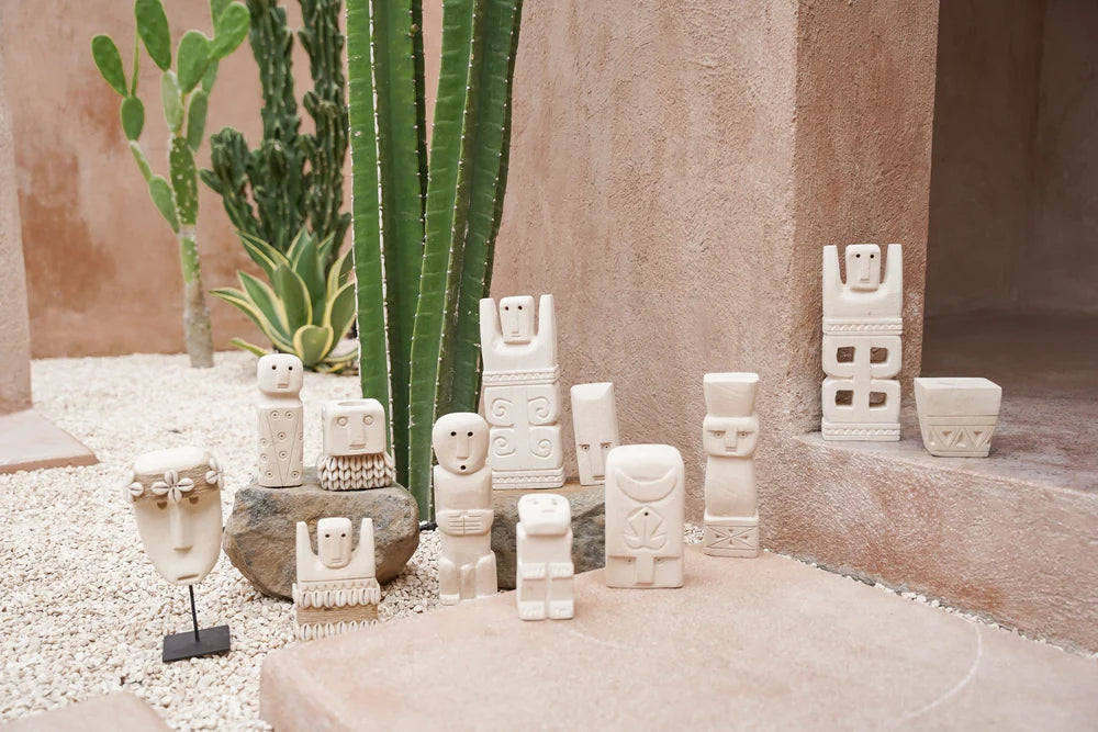 Kayu Living handmade stone guardian figurines from Bali displayed on gravel with cactus plants in a desert setting.
