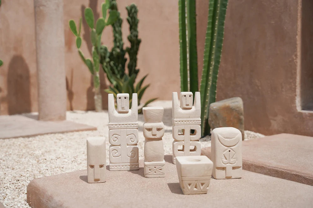 Kayu Living handmade stone guardian figurines from Bali with unique carved faces displayed on a sandy desert surface.