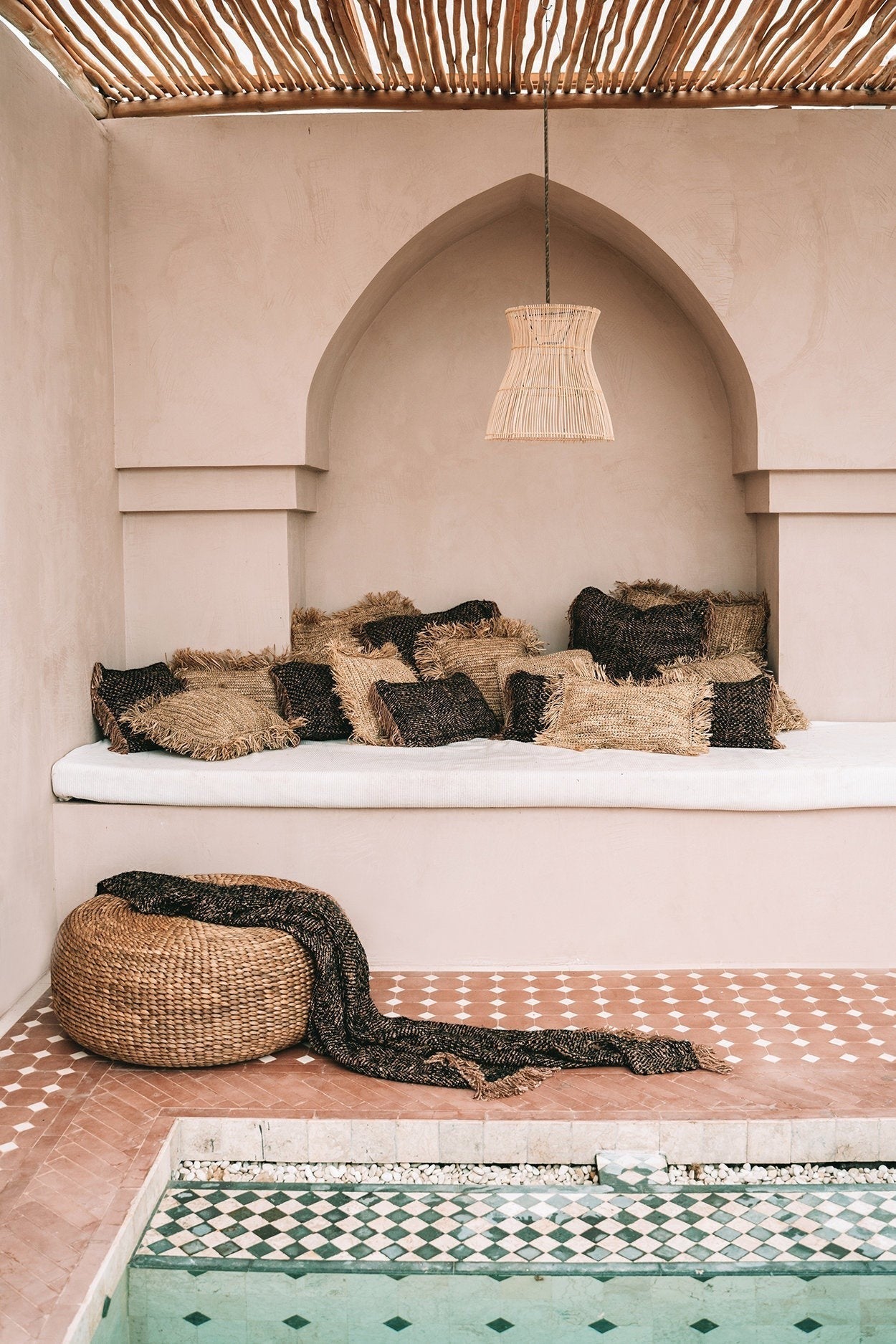 Kayu Living natural water hyacinth pouf with a black throw blanket in a Mediterranean-style outdoor lounge area.