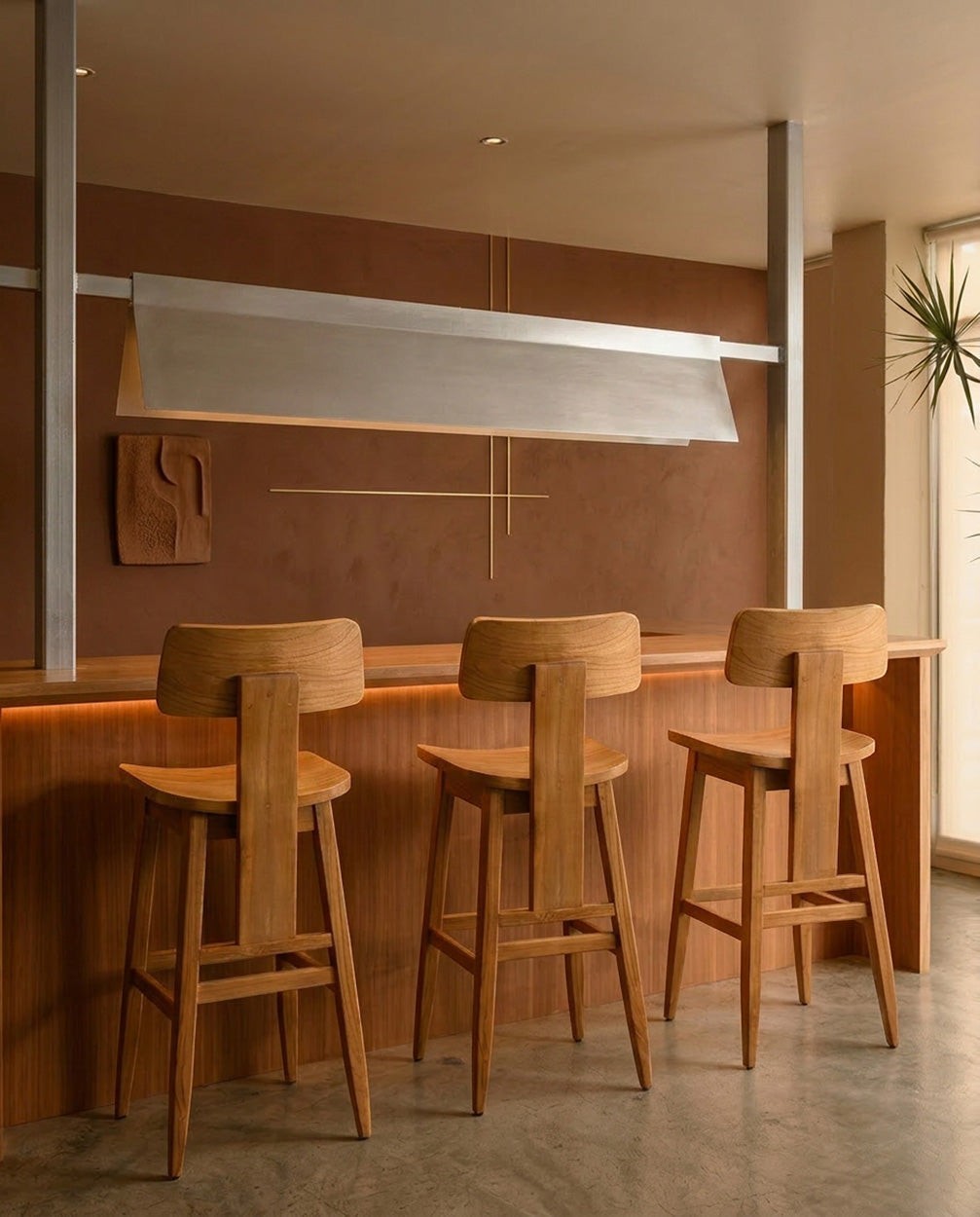Kayu Living LovYa teak barstools with modern curved backrests in a warm, minimalist dining room setting.