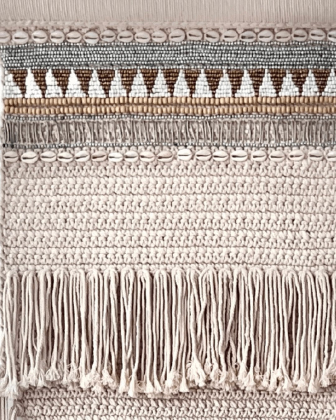 Kayu Living macrame wall hanging with beads, shells, and fringe. Beige crochet texture with geometric patterns.