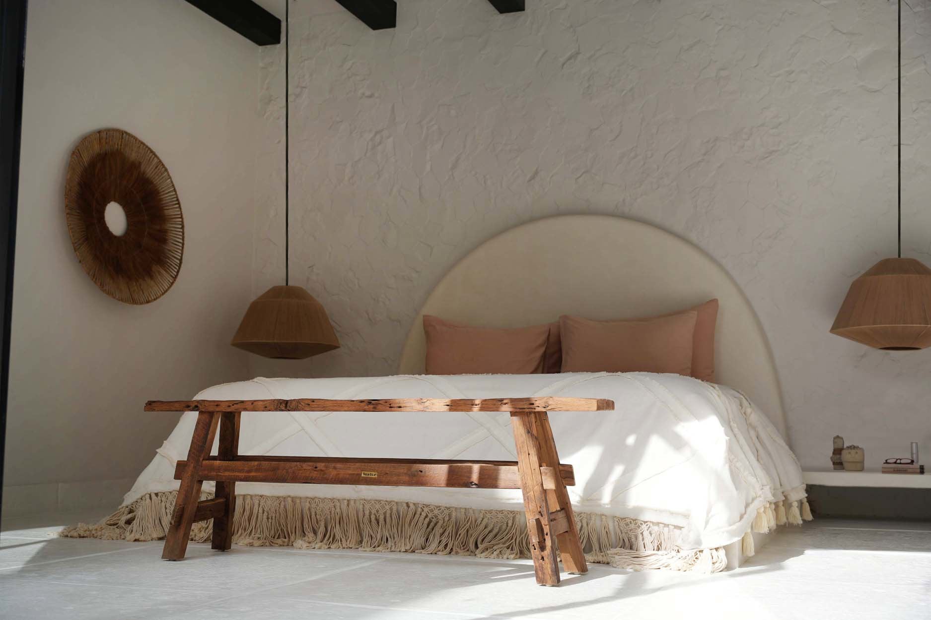 Kayu Living natural Berber cotton bed throw with fringe detail draped over a rustic wooden bench in a bedroom