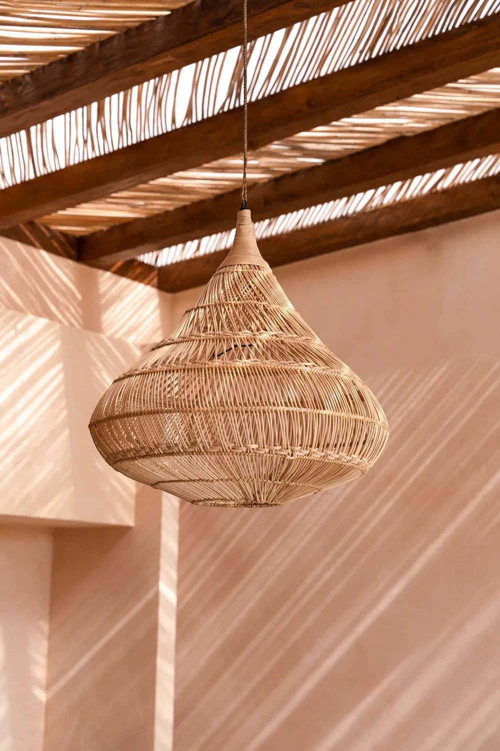 Kayu Living teardrop pendant lamp made of natural rattan with intricate weave, creating ambient light and shadows.