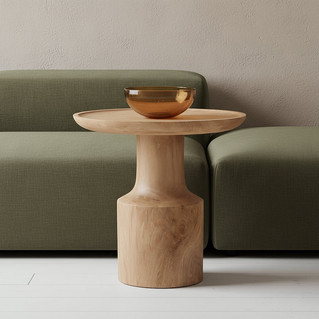 Kayu Living Nero Day side table in natural teak wood with a pedestal base, placed in front of a green sofa.