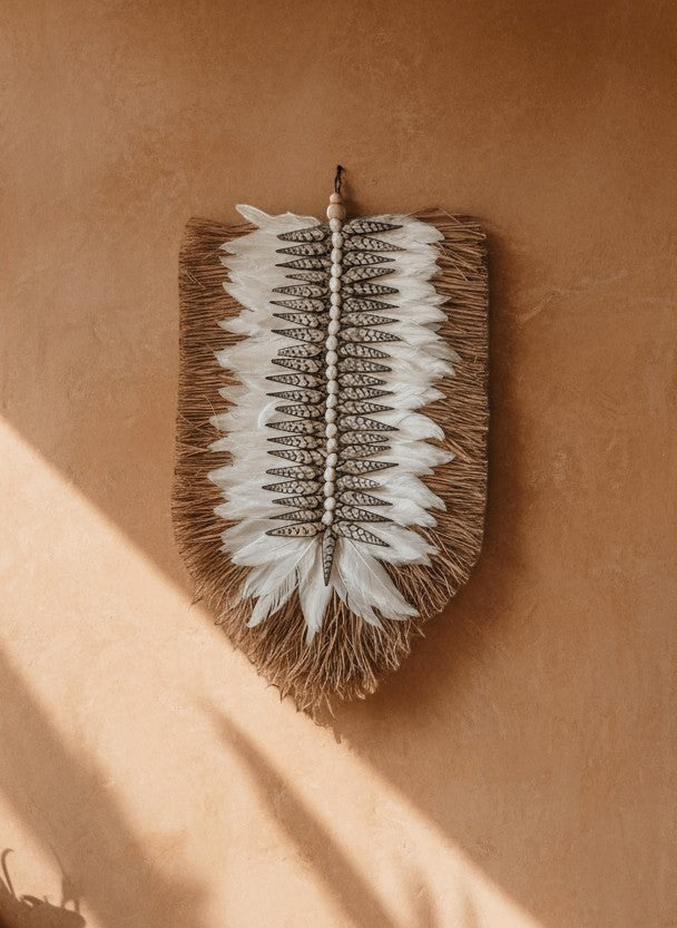 Kayu Living Nias feather and shell wall decoration with natural fibers and beaded accents. White feathers and shells create a central pattern.