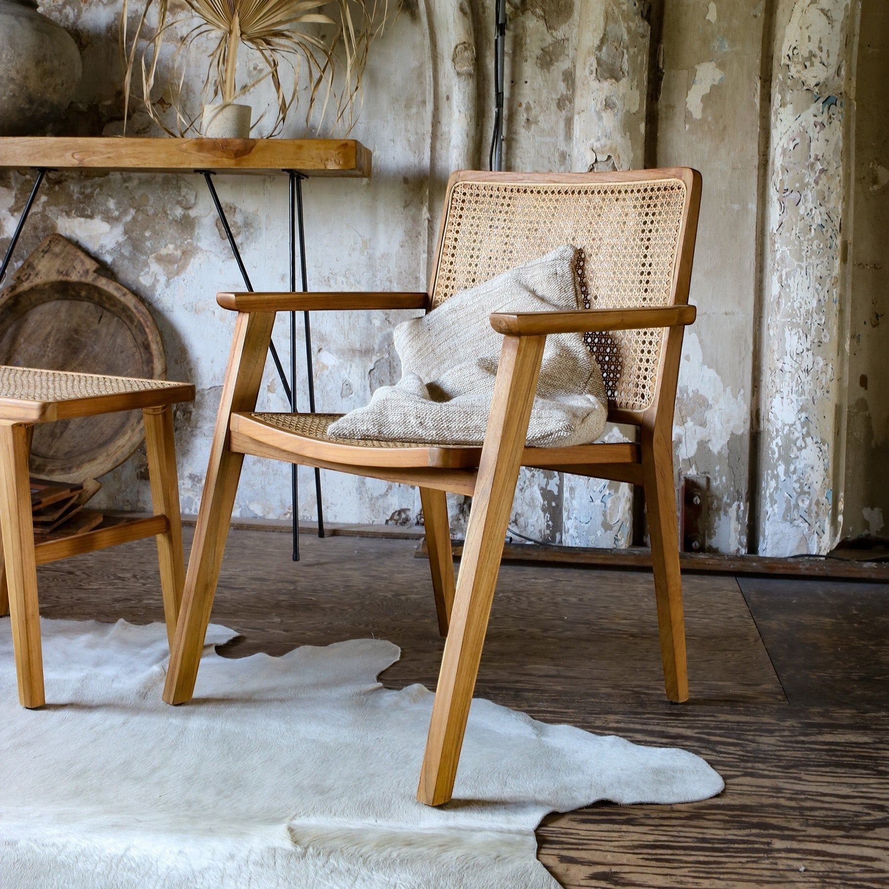 Kayu Living Nova teak dining chair with armrests and hand-woven rattan seat and back in a rustic interior setting.