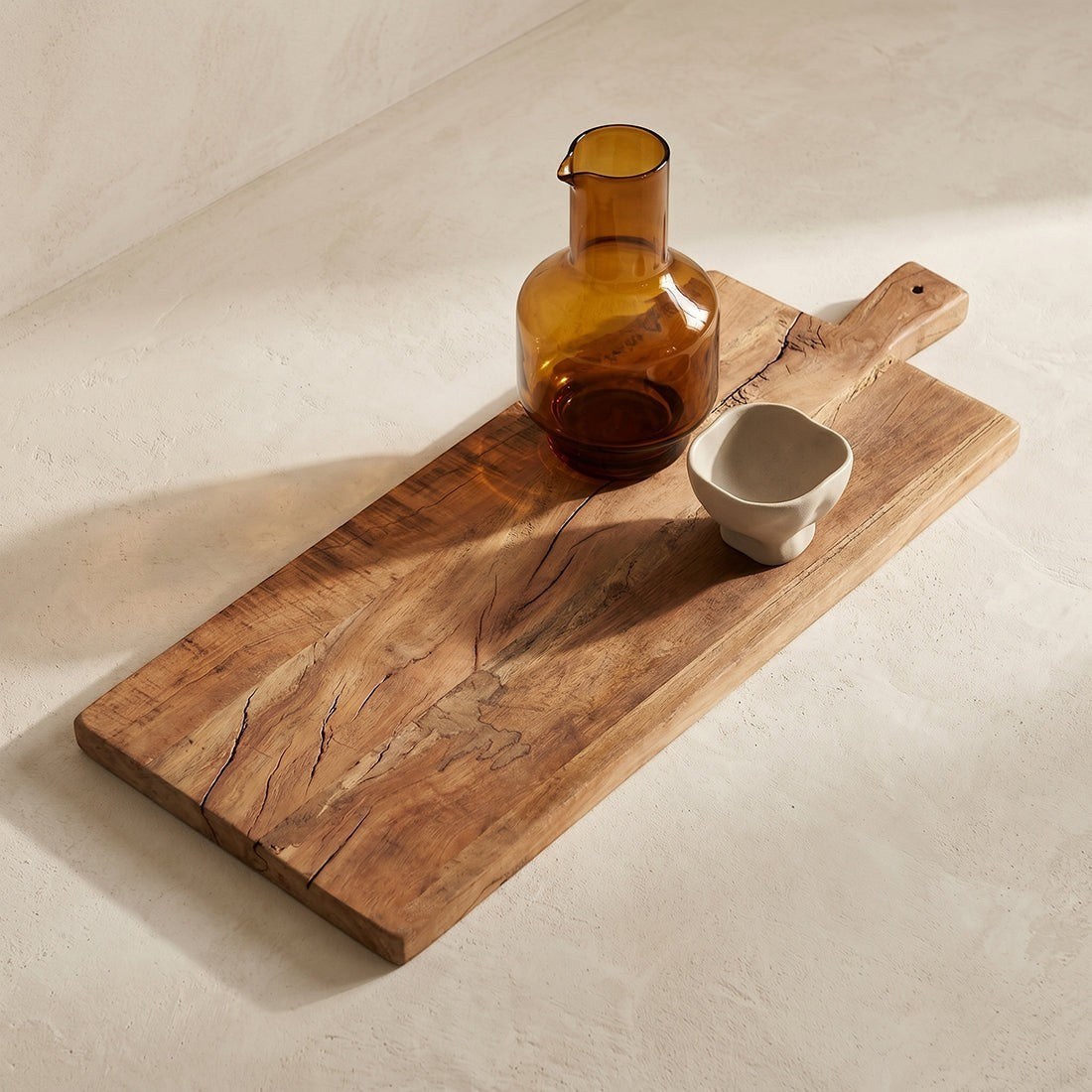 Kayu Living 60 cm reclaimed wood charcuterie board with natural grain, featuring an amber glass carafe and small bowl.