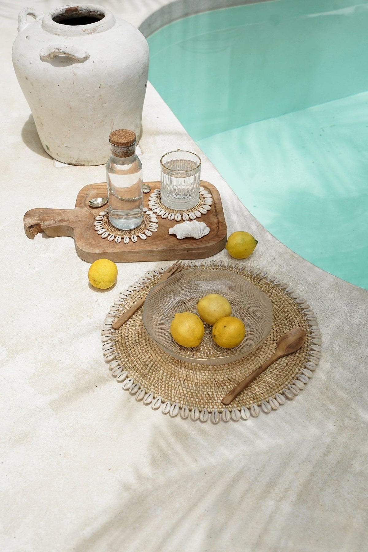 Kayu Living gold brass shell spoon placed on a woven placemat with lemons by a swimming pool