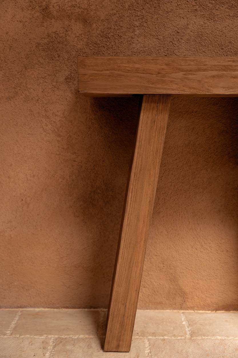 Kayu Living Stance Console table in natural teak wood with clean angular design against a textured terracotta wall.