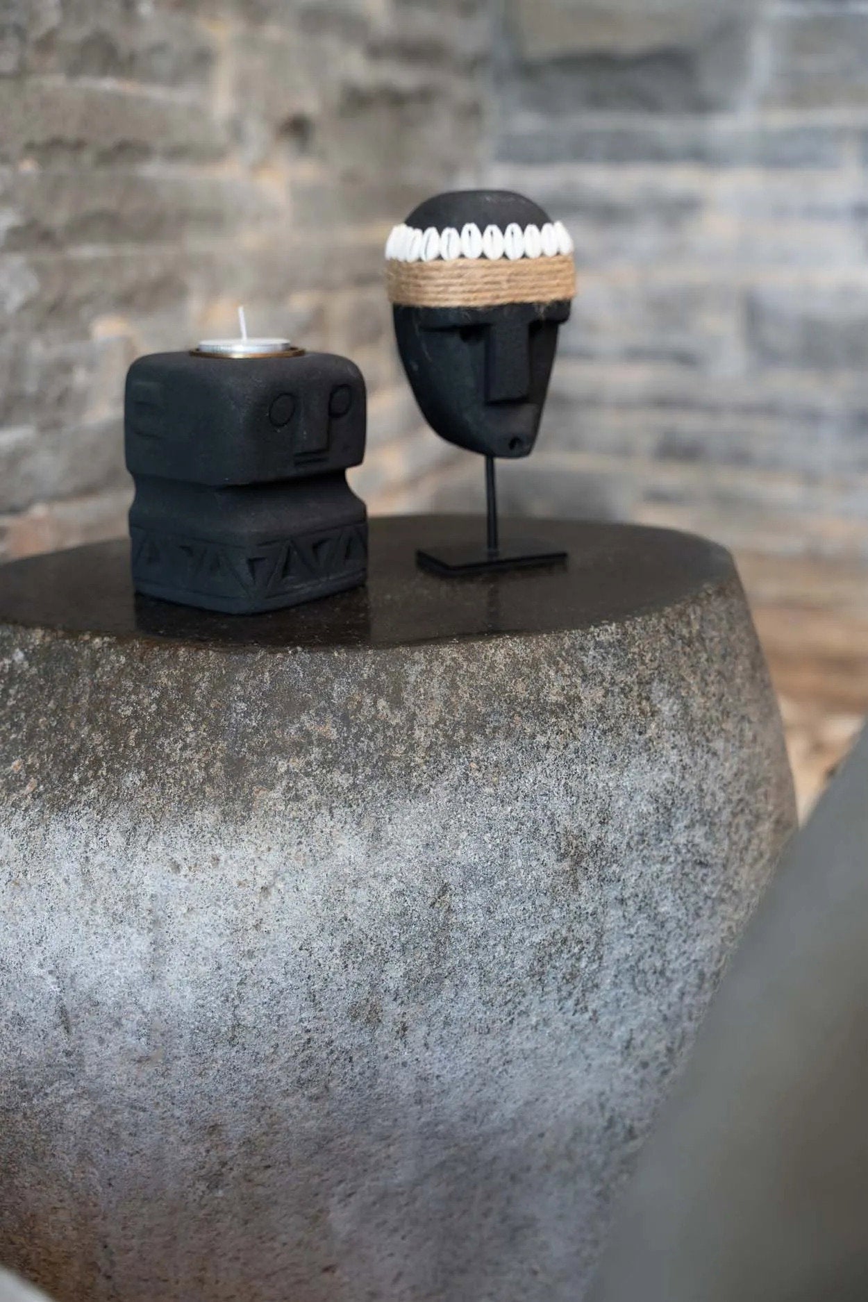 Kayu Living hand-carved black sandstone Sumba statue on a metal stand displayed with a matching stone candle holder.