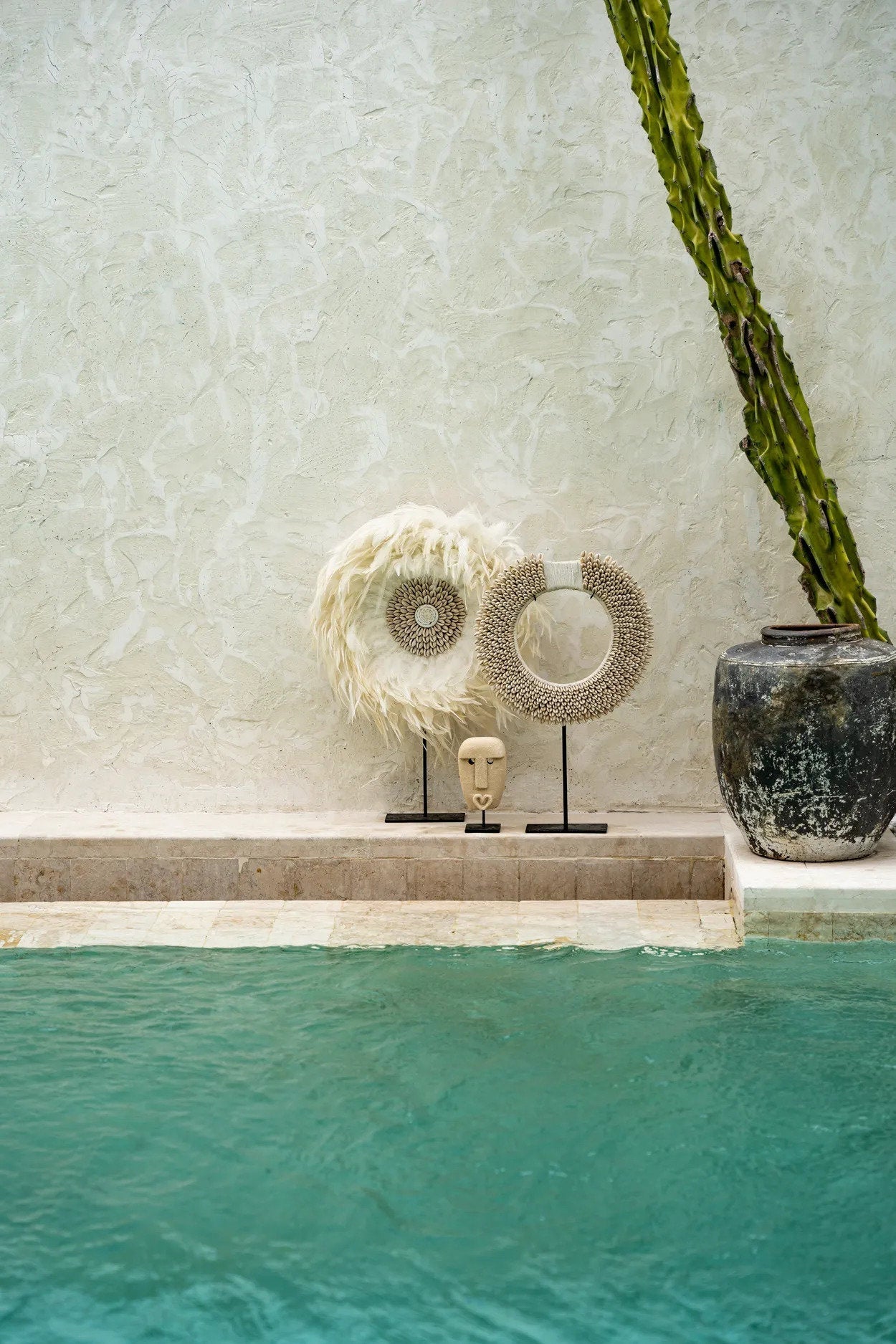 Kayu Living hand-carved sandstone Sumba stone statue on a metal stand, displayed by a pool with tribal decor.