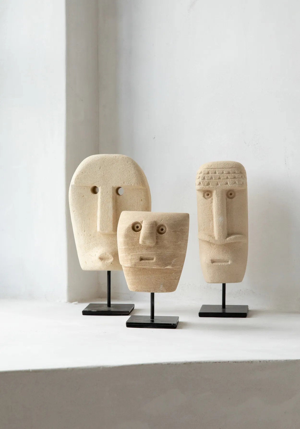 Kayu Living hand-carved sandstone Sumba stone statues on black metal stands, featuring unique tribal face designs.