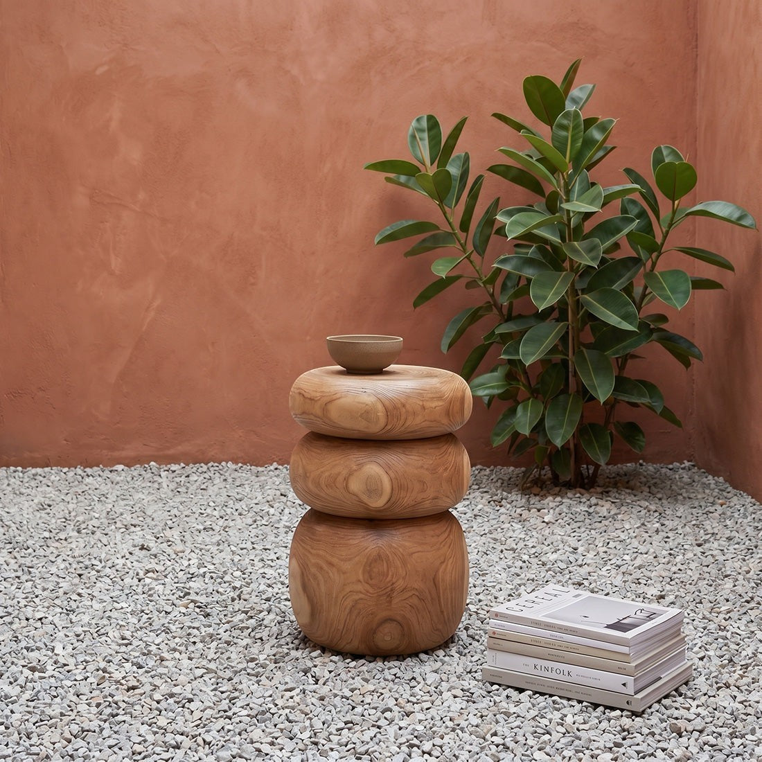 Kayu Living Tao teak side table with rounded stone-like shapes, placed on gravel next to a potted plant.