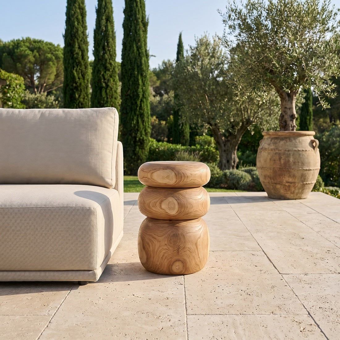 Kayu Living Tao teak side table with rounded stone-like design on a sunny outdoor terrace next to a beige sofa.