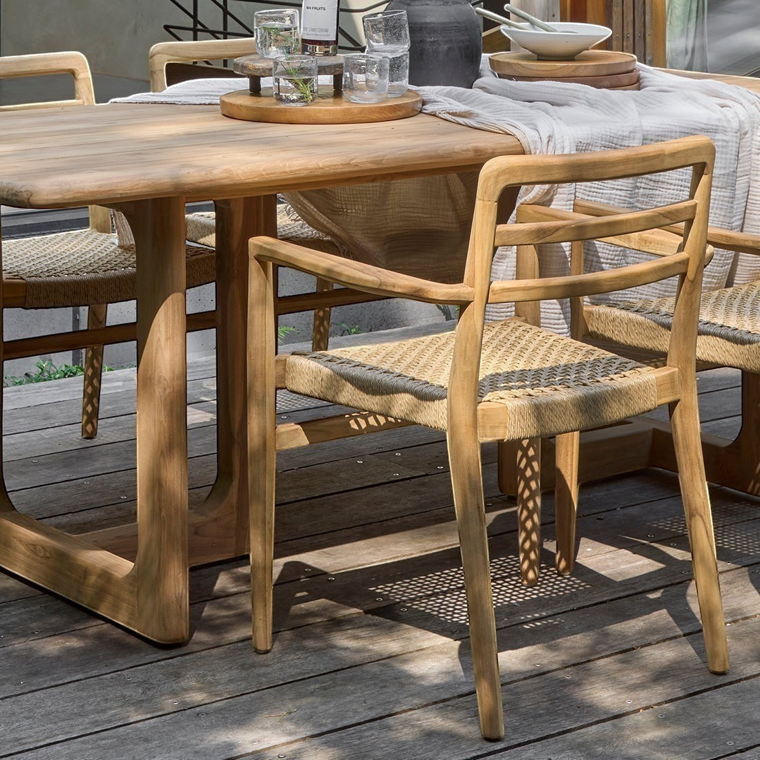 Kayu Living Verano teak garden chair with armrests and woven rope seat on a wooden patio dining set