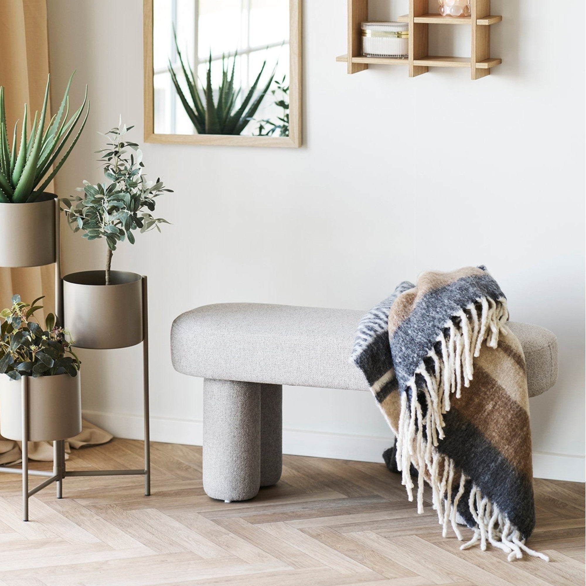Kayu Living Weston Bench in light grey upholstery with unique curved legs and a neutral plaid throw. Minimalist design.