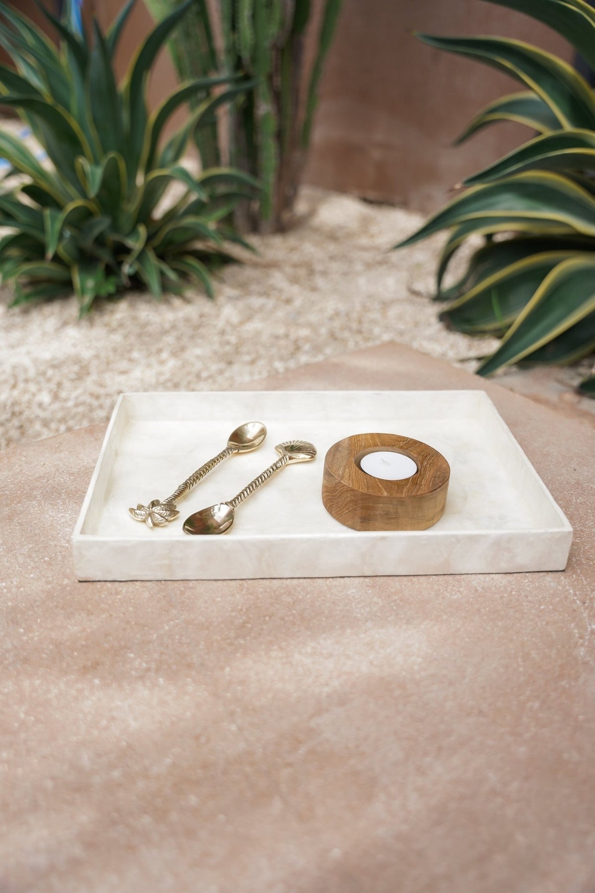 Kayu Living white rectangular Capiz shell tray holding two gold spoons and a wooden candle holder on a stone surface.