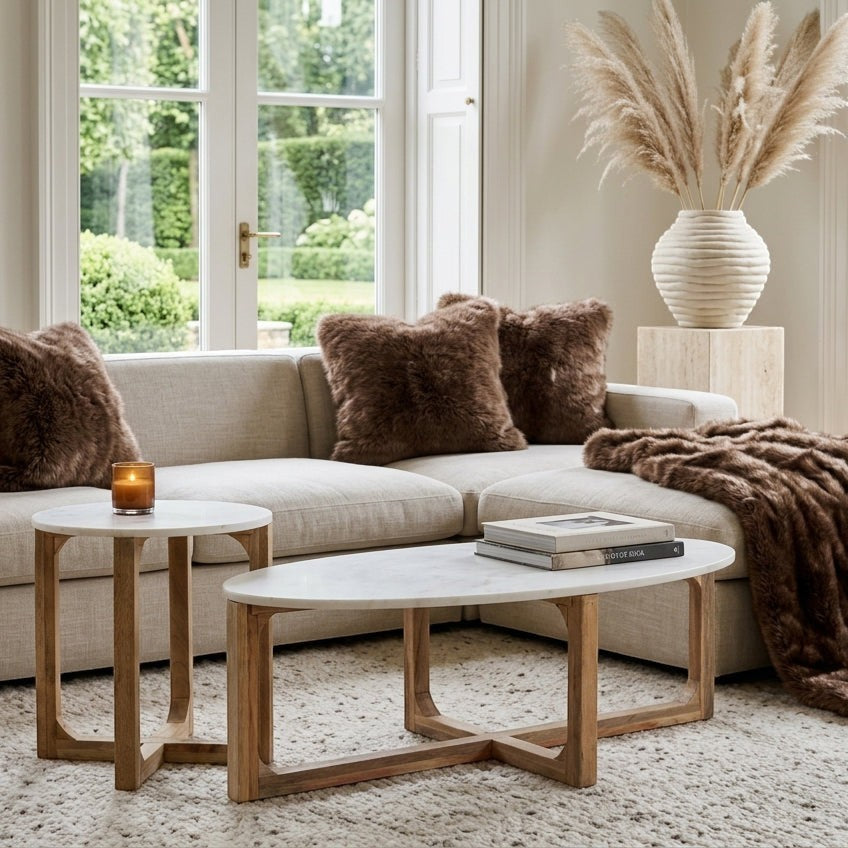 Kayu Living white marble side table with mango wood cross base next to a matching oval coffee table in a living room