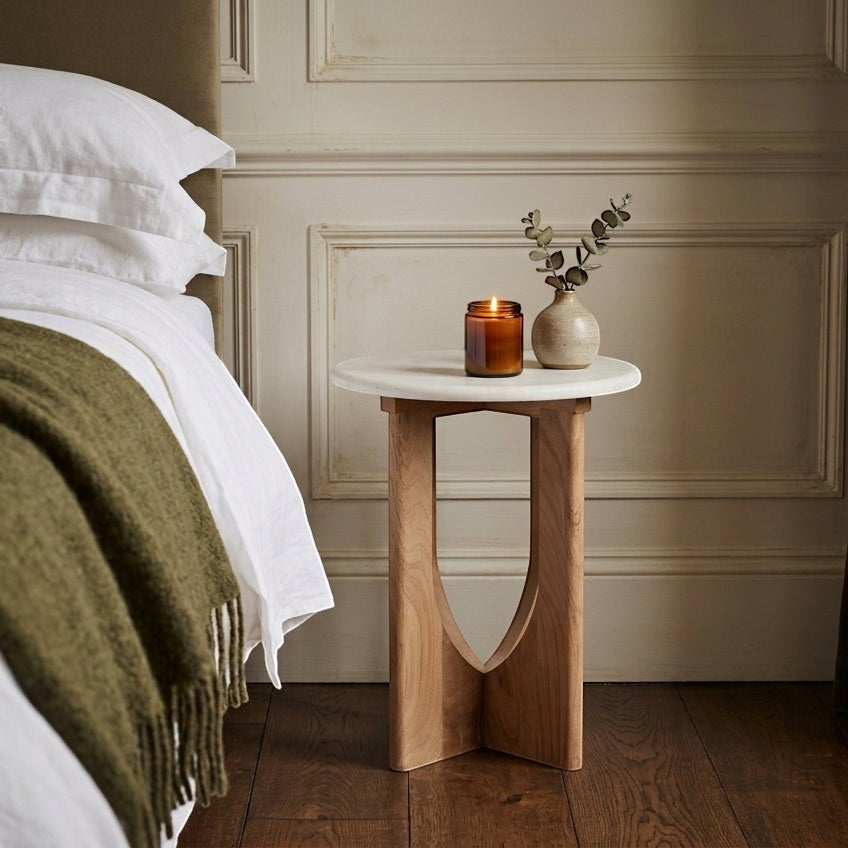 Kayu Living white marble side table with arched mango wood base styled as a bedside table with a candle and vase.