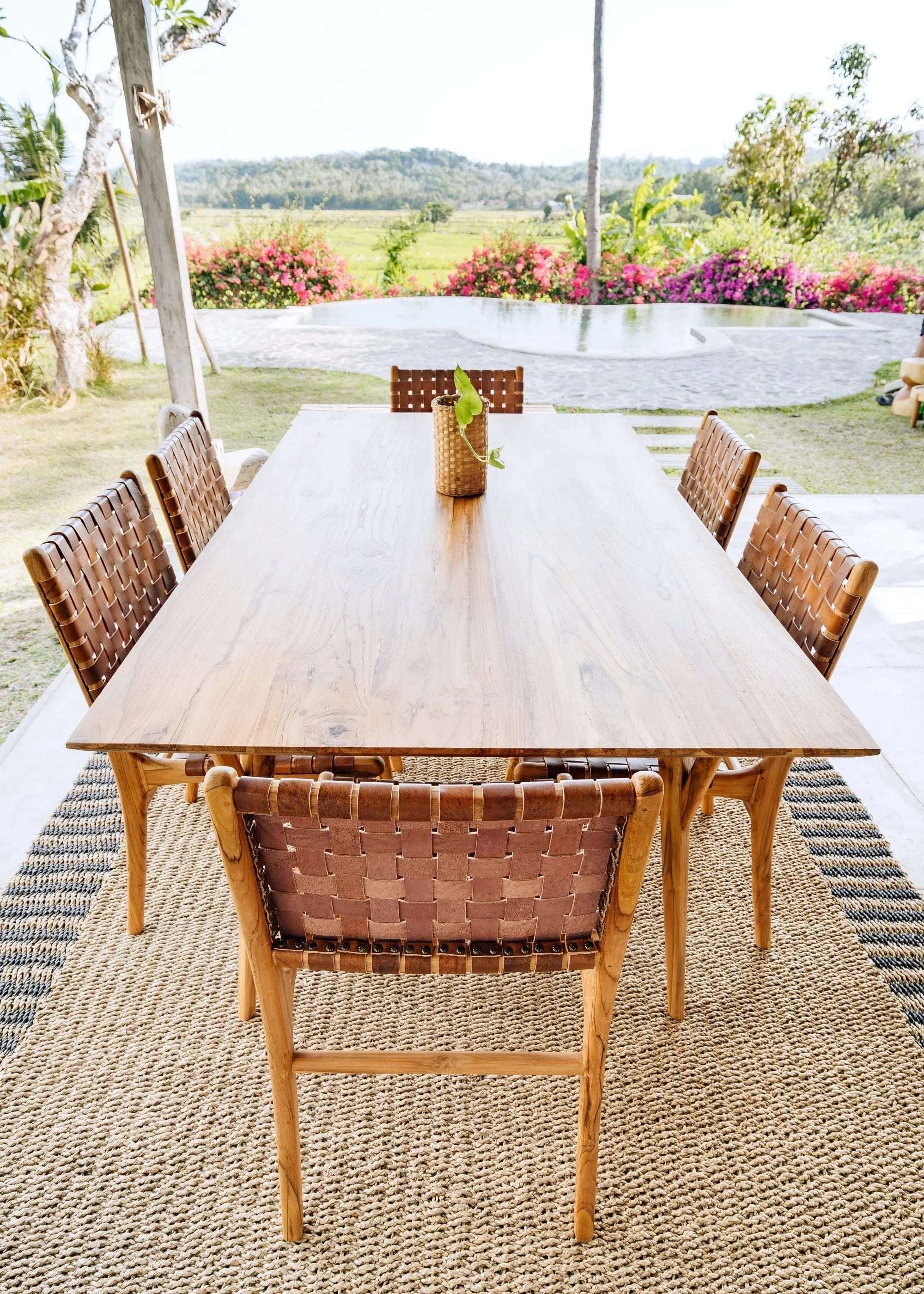Handcrafted wooden dining table with woven chairs by Kayu Living on a natural fiber rug outdoors