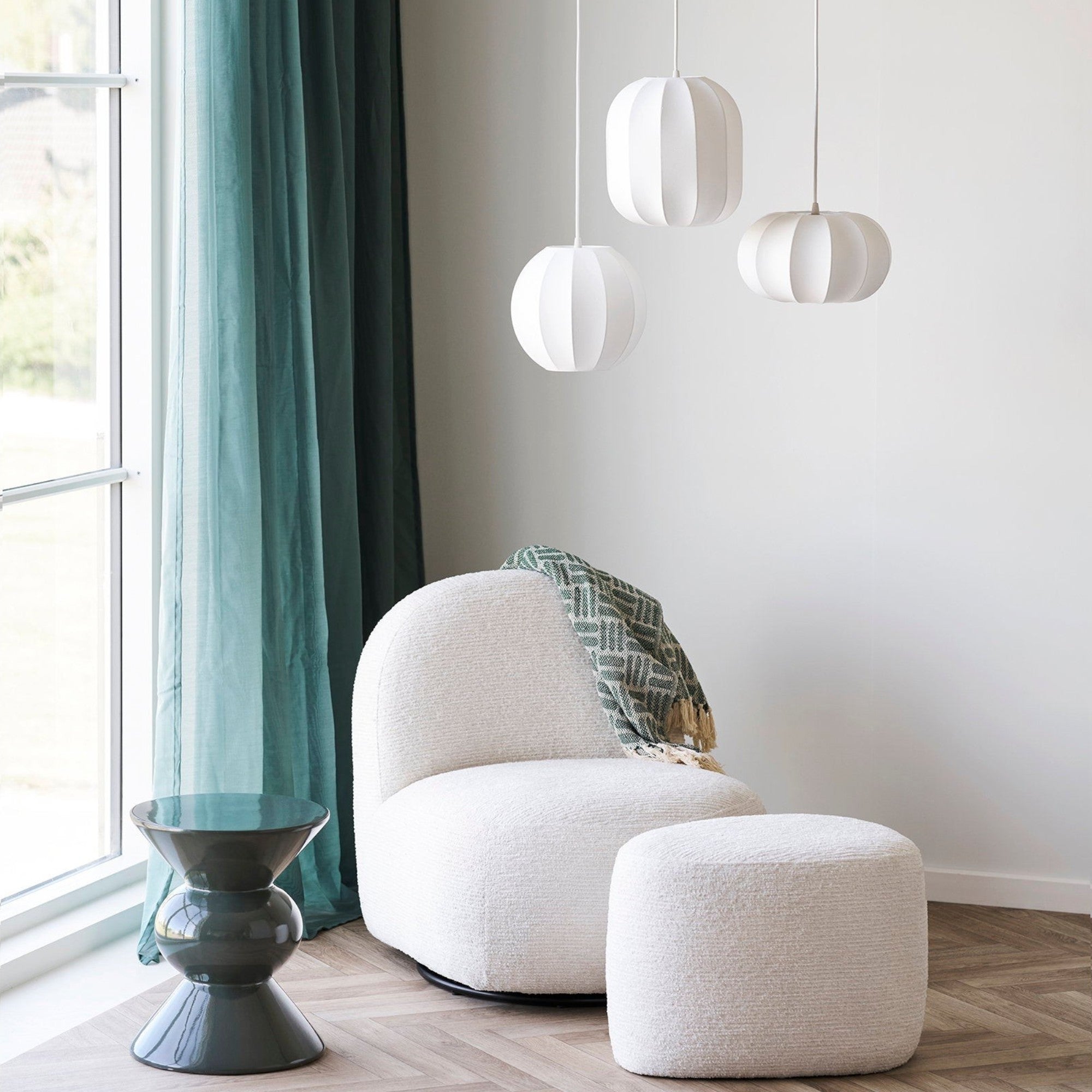 Kayu Living Adana green plaid throw blanket draped over a white boucle armchair in a bright, modern living room.