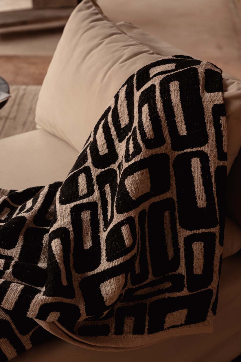 Kayu Living Aztec-pattern cotton bed throw in natural black draped over a sofa for a cozy, textured look.