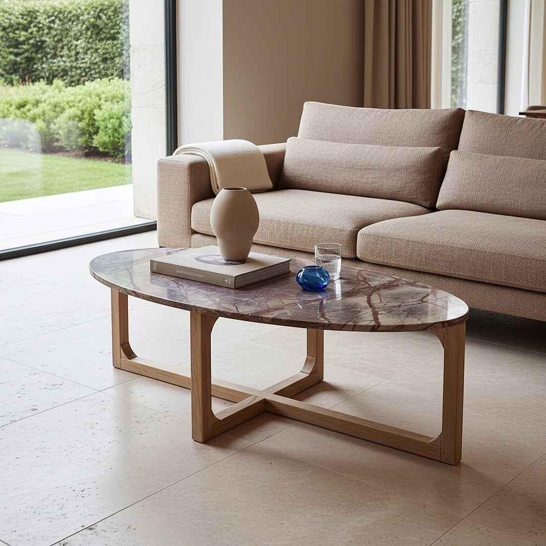 Kayu Living Bizar oval marble coffee table with unique veining and a light mango wood cross-frame in a living room.
