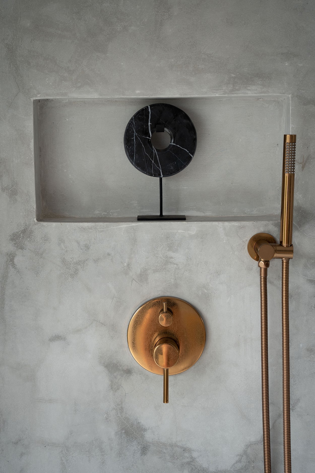 Kayu Living black marble disc sculpture on a metal stand displayed in a concrete shower niche with brass fixtures.