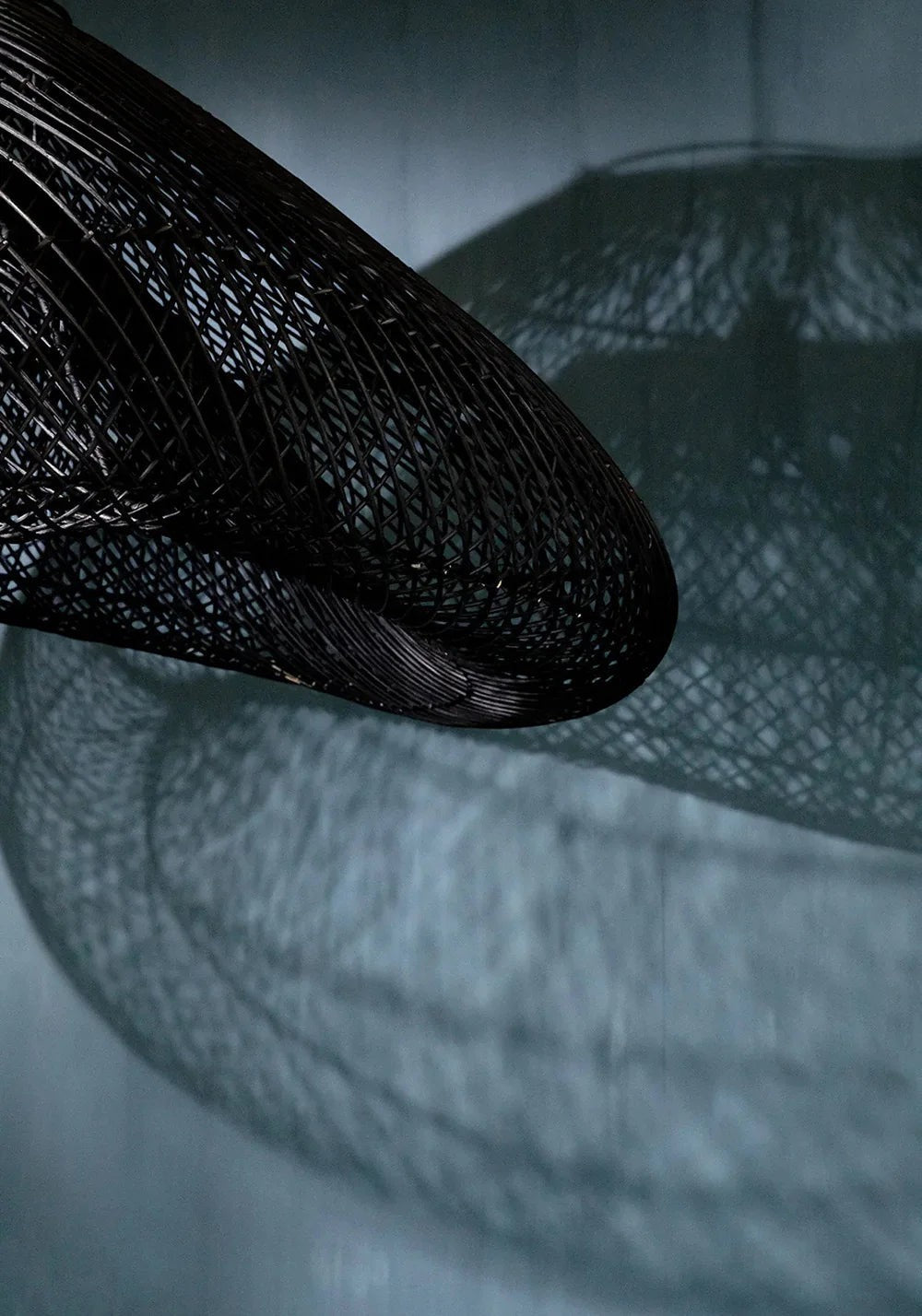 Kayu Living black oversized rattan pendant lamp with a sculptural, flowing form and intricate weave casting a shadow.