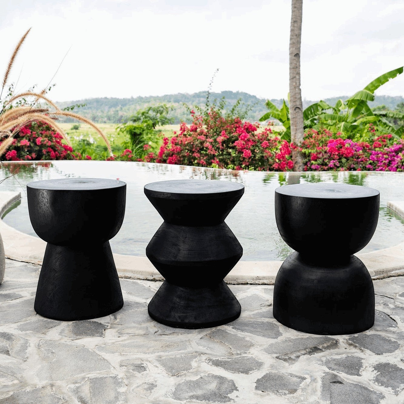 Kayu Living black hourglass stool made from solid suar wood, handmade by artisans in Java. Unique grain and rustic character.