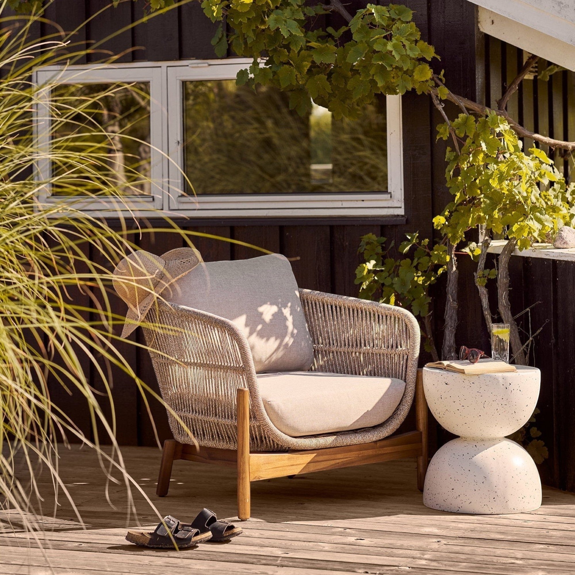 Kayu Living Bonita off-white fiberclay side table with a terrazzo finish on a wooden deck next to a lounge chair.
