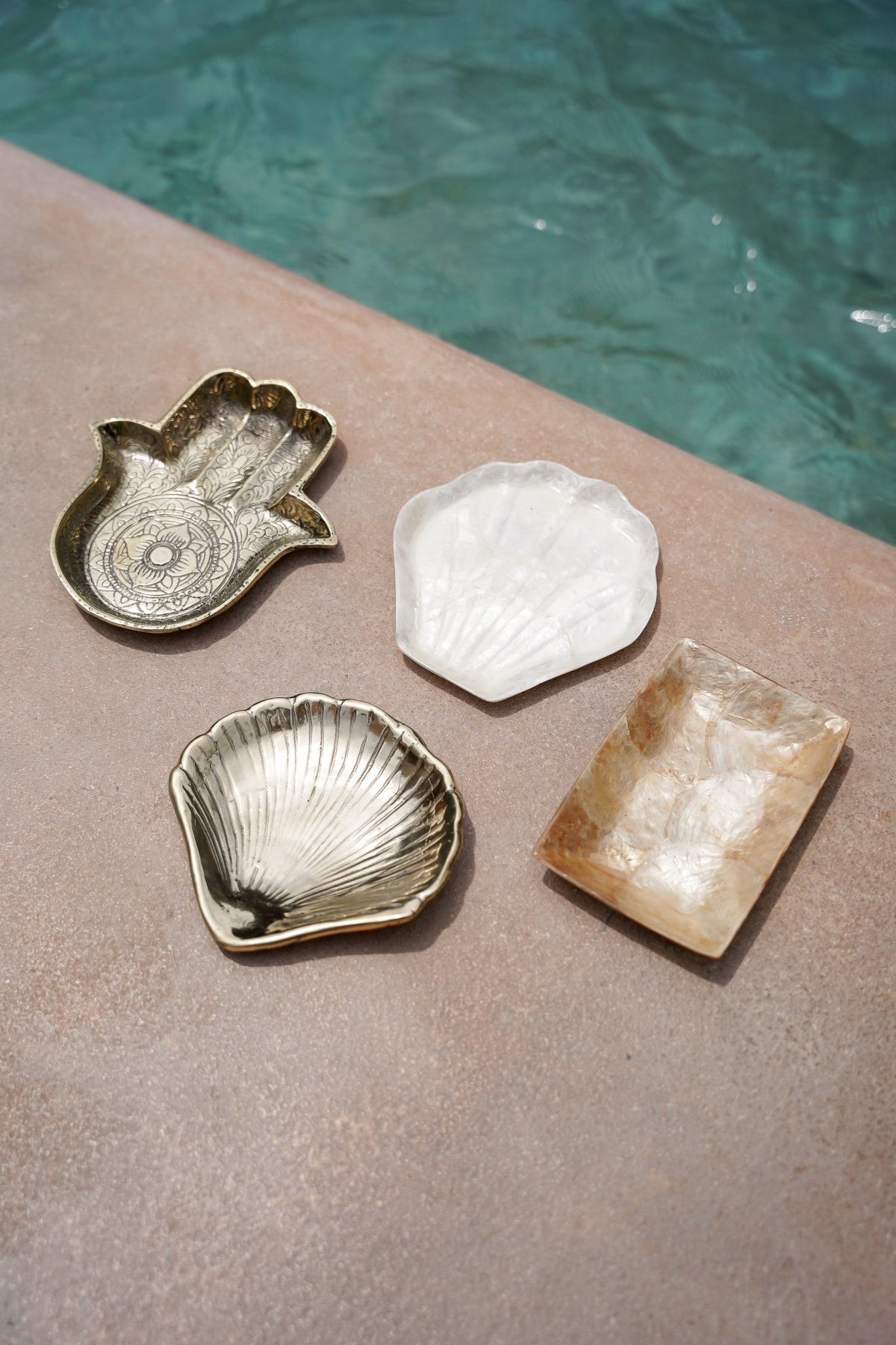 Kayu Living handmade brass shell dish alongside a hamsa tray and decorative stone plates on a poolside ledge.