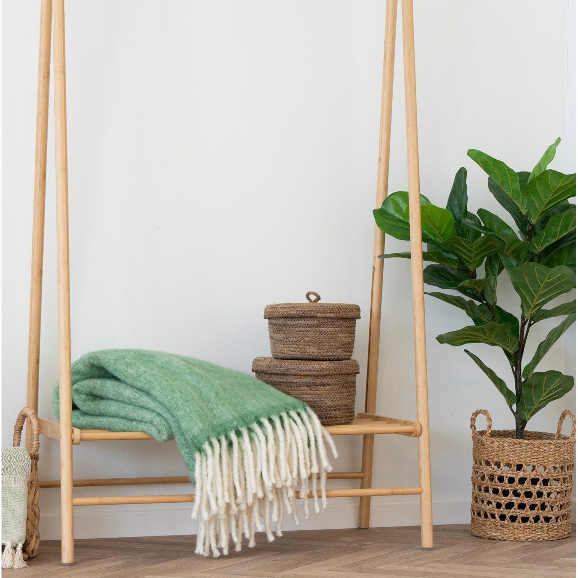 Kayu Living Carmel green wool-blend throw blanket with fringe, draped on a wooden rack in a cozy room setting.