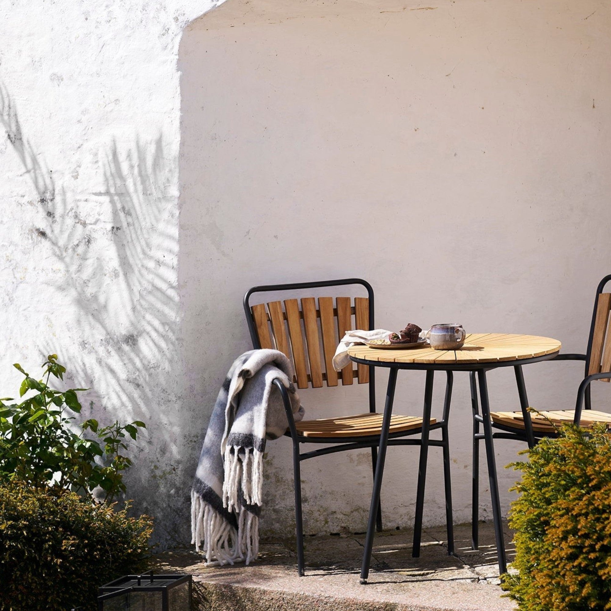 Kayu Living Carmel Plaid wool-blend throw in grey and white draped over a wooden garden chair on a sunny patio.