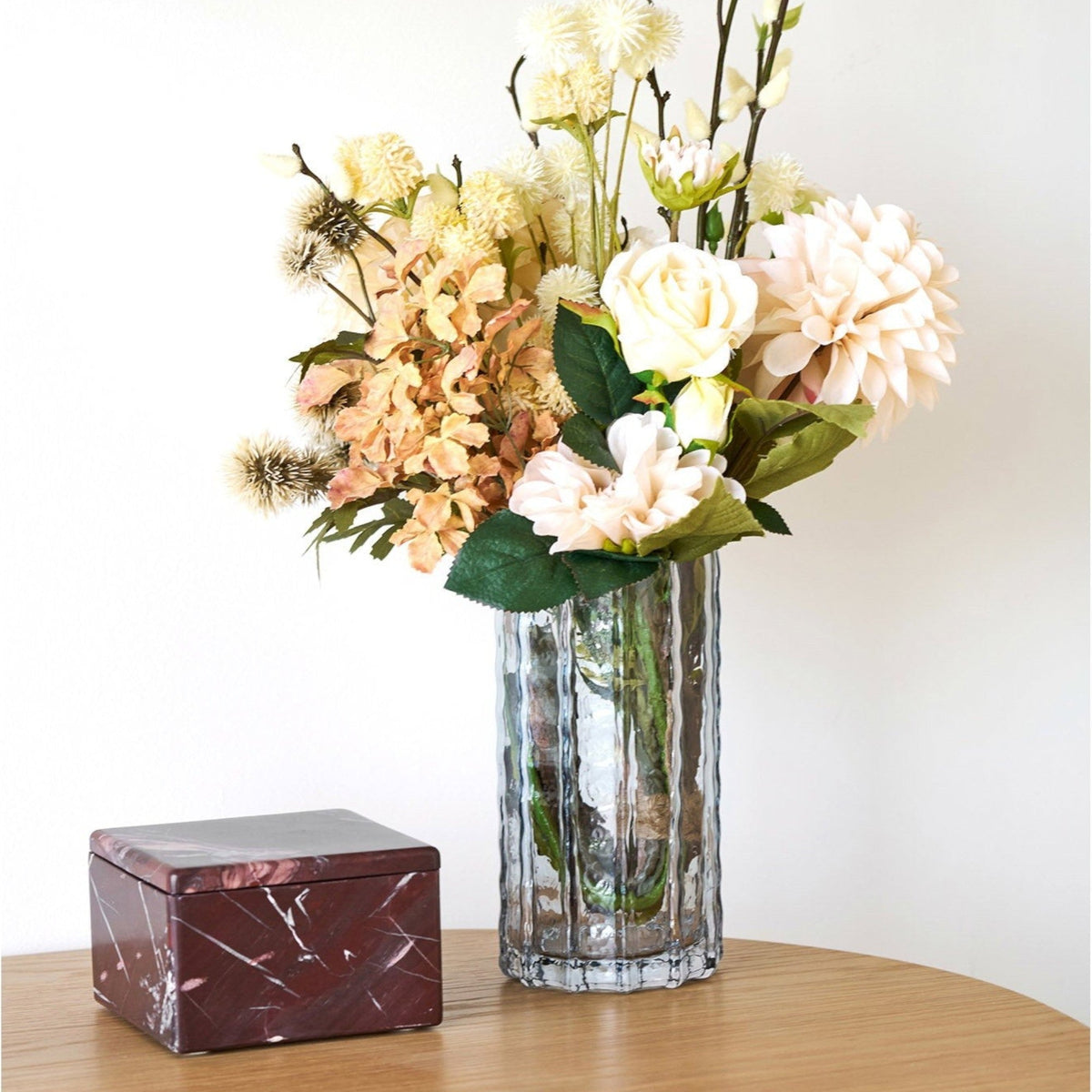 Kayu Living chestnut-red marble jar with a polished finish sitting on a wooden table next to a glass flower vase