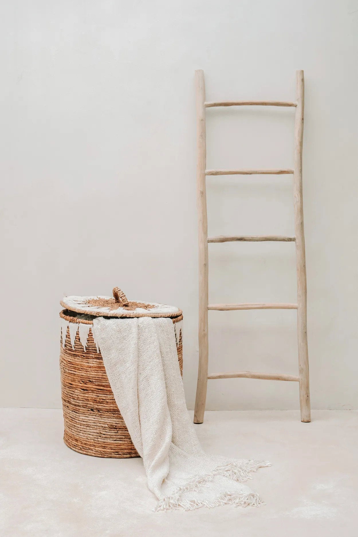 Kayu Living cream hand-woven cotton throw with fringe draped over a woven basket next to a wooden ladder