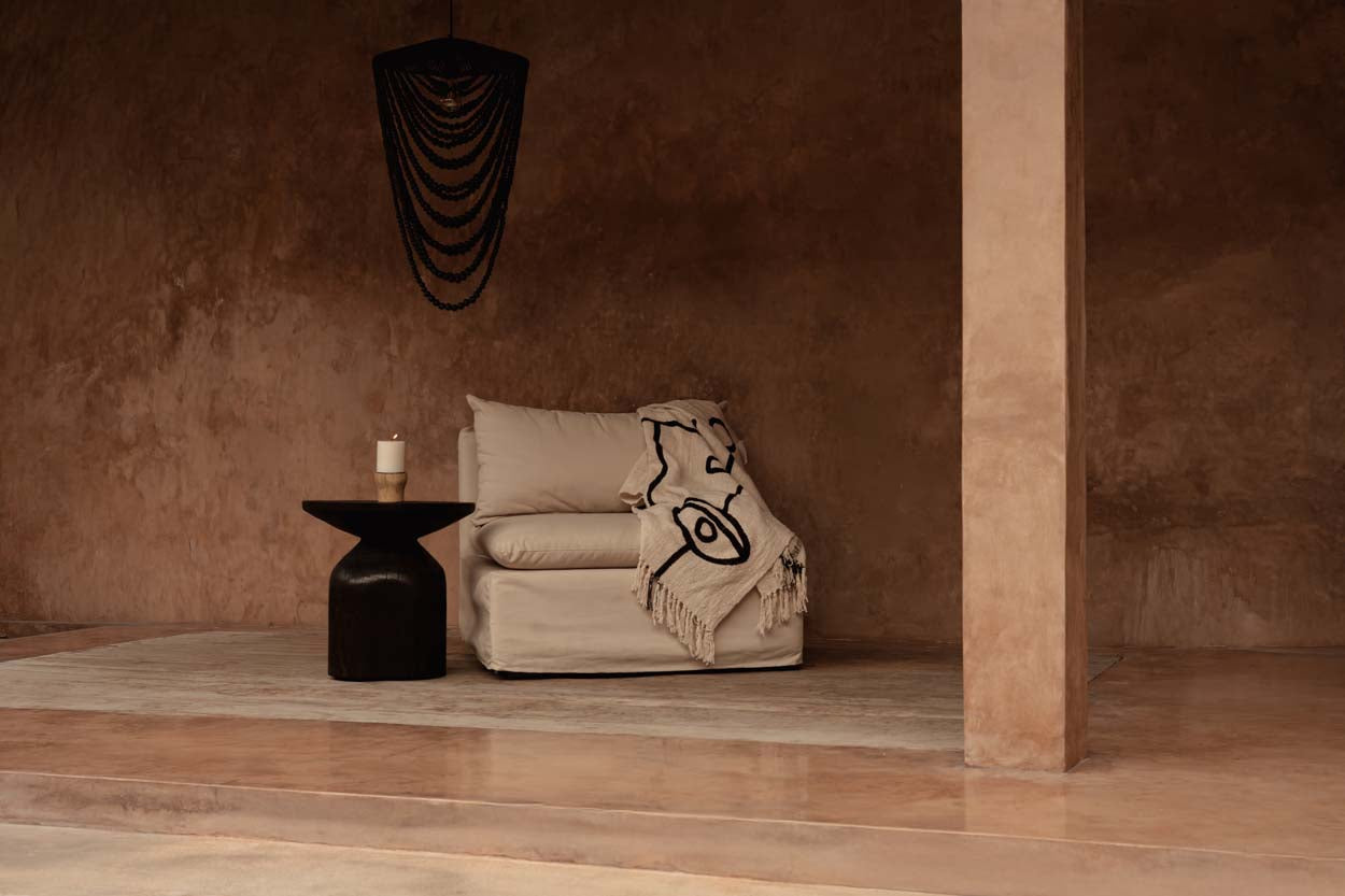 Kayu Living natural black cotton plaid bed throw with evil eye motif draped over a modern beige armchair