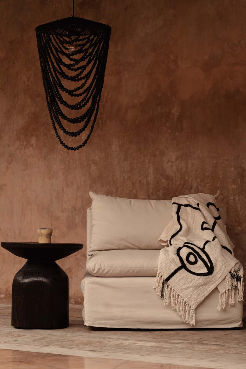 Kayu Living natural black cotton bed throw with evil eye motif draped over a beige sofa in a rustic room