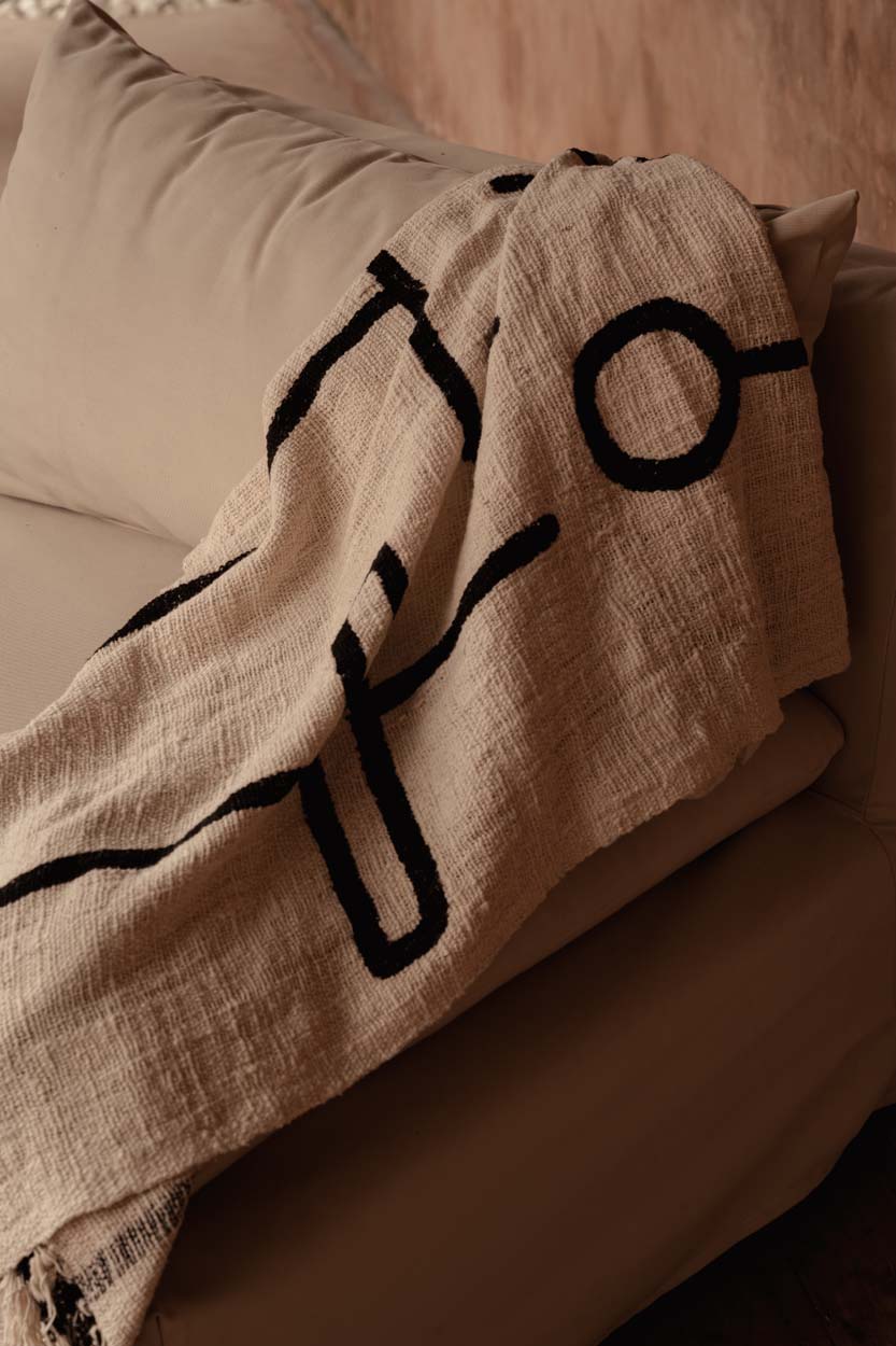 Kayu Living natural black cotton bed throw with evil eye pattern draped over a sofa